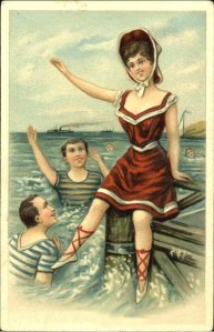 1908 girl in a skirted bathing costume having fun on a dock while two admiring boys splash in the water below.